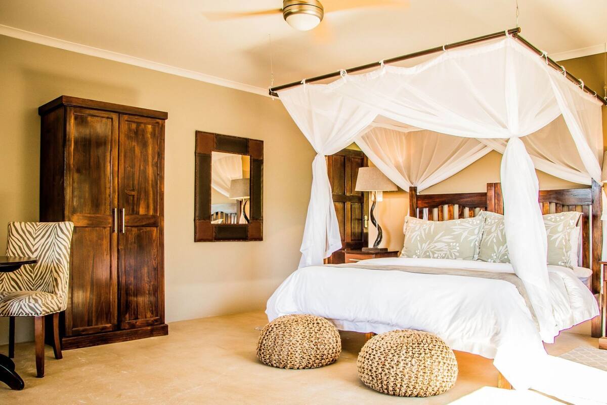 A bedroom with a four-poster bed, a wooden wardrobe, a chair, and a mirror.