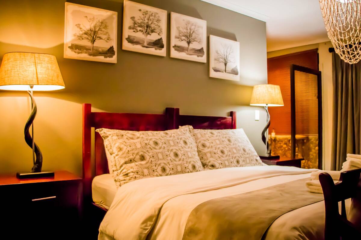 A neatly made bed with a red headboard, two bedside lamps, and three framed pictures on the wall.