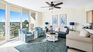 A spacious living room with a large sliding glass door leading to a balcony, a ceiling fan, and a view of the ocean. - Recently Renovated Two Bedroom With Gorgeous Water Views! Complimentary Boat Slip! (Orange Beach)