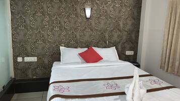 A neatly made bed with white bedding and a red pillow, a wall with ornate patterned wallpaper, and a light switch on the wall.