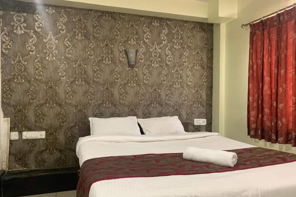Una habitación de hotel con una cama grande, un cabecero decorativo, una lámpara de pared y una cortina roja.