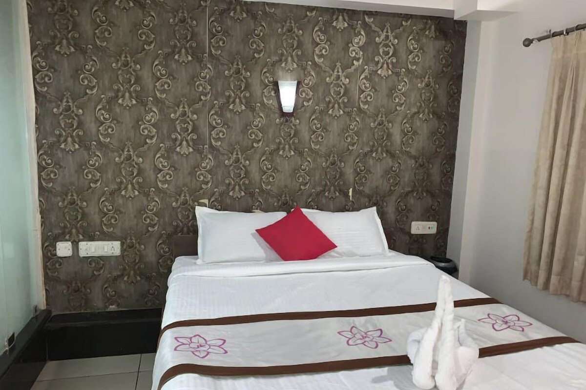 A hotel room with a patterned headboard, a bed with white bedding and a red pillow, and a swan decoration on the bed.