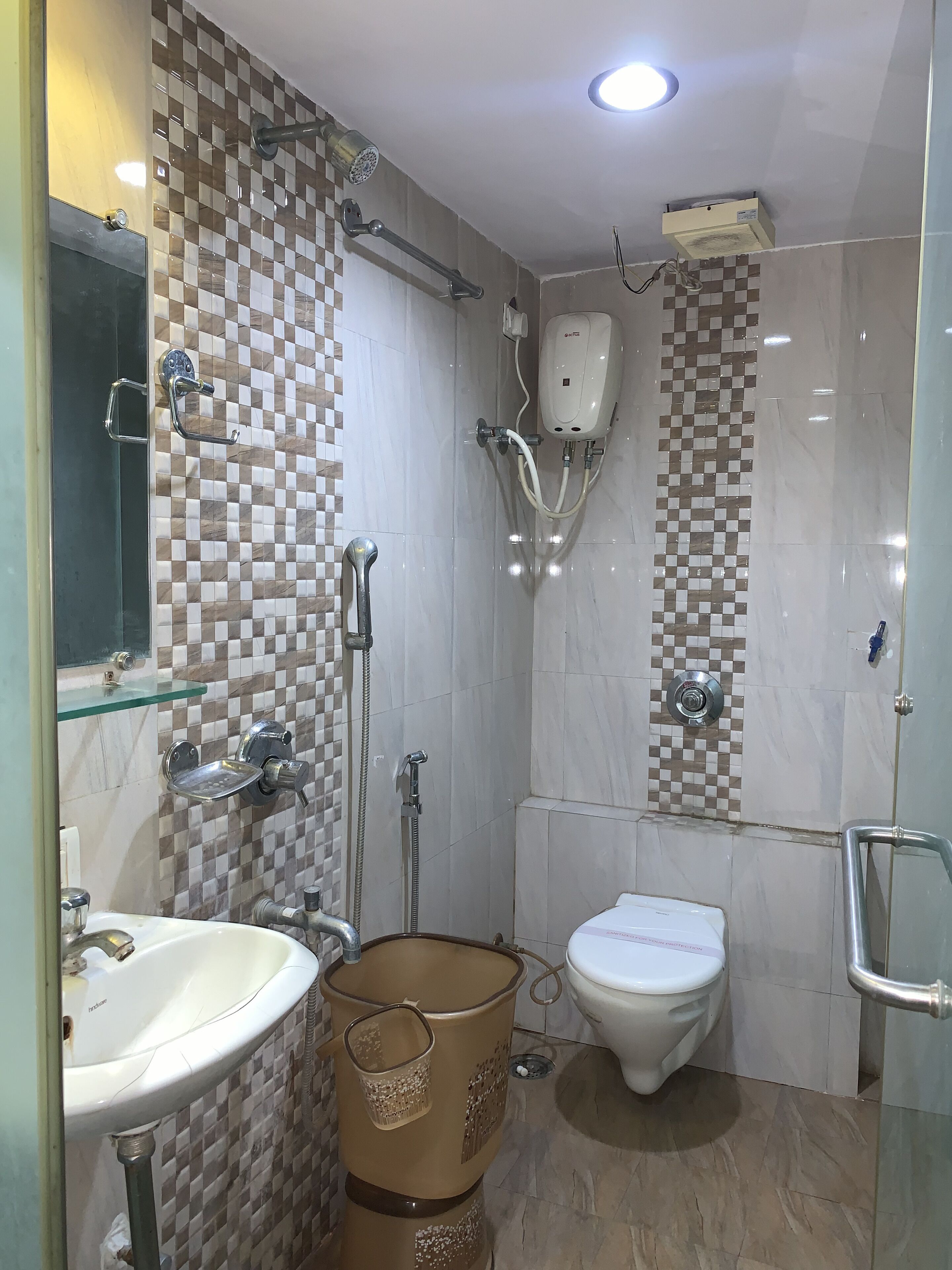Un baño con pared de baldosas a cuadros, cabina de ducha de vidrio, inodoro y lavamanos.