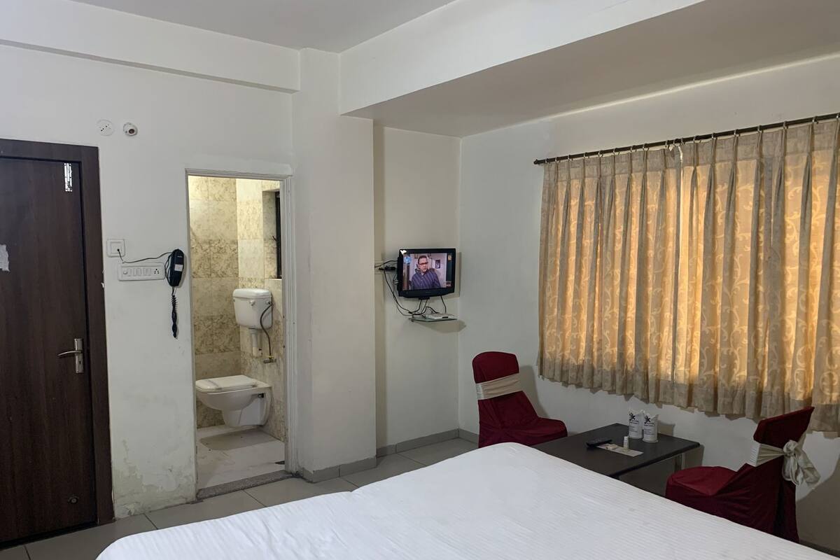Una habitación de hotel con cama, televisor, escritorio con silla, baño y puerta.