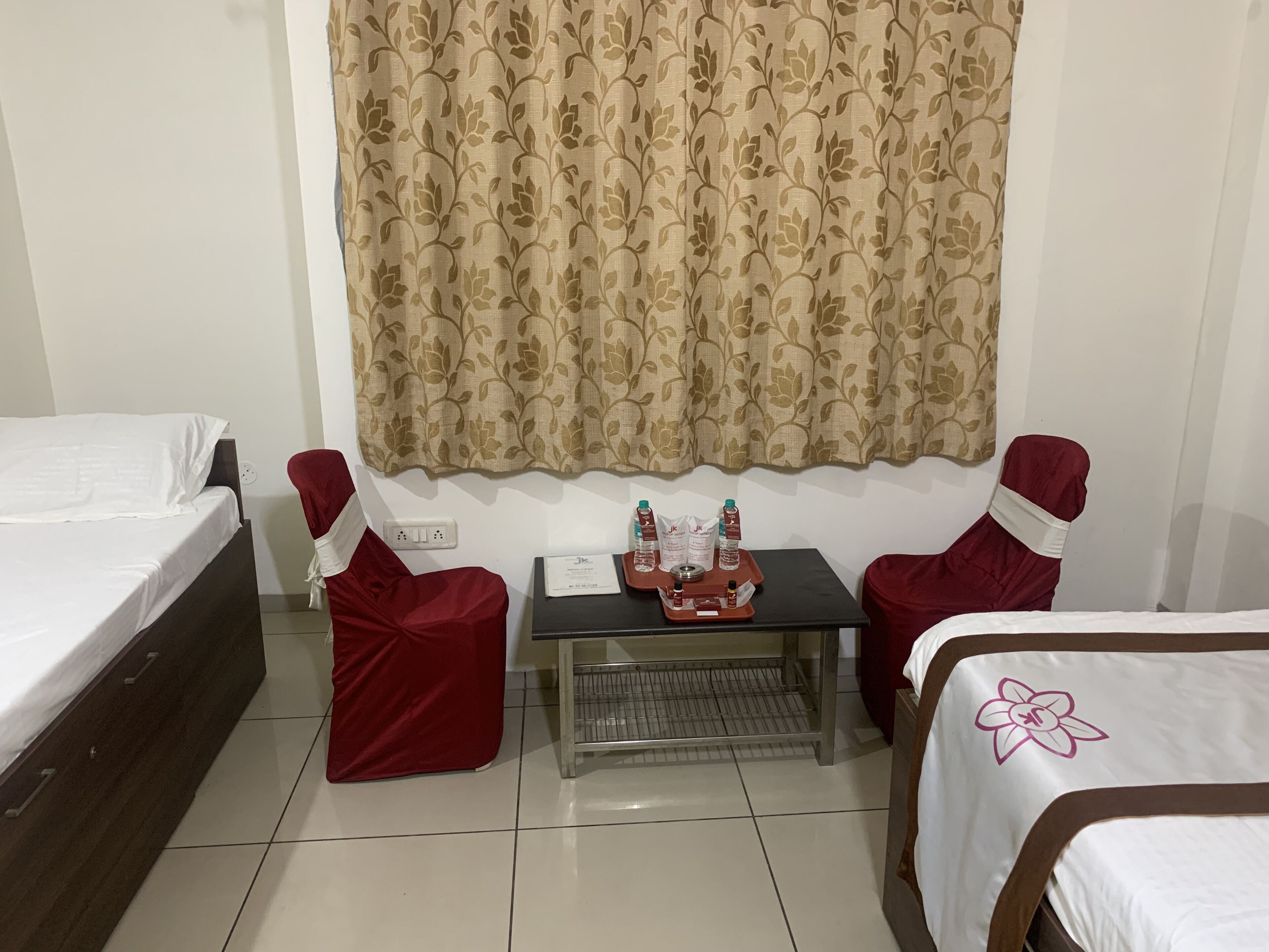 A hotel room with two single beds, a small table with toiletries, and a chair.