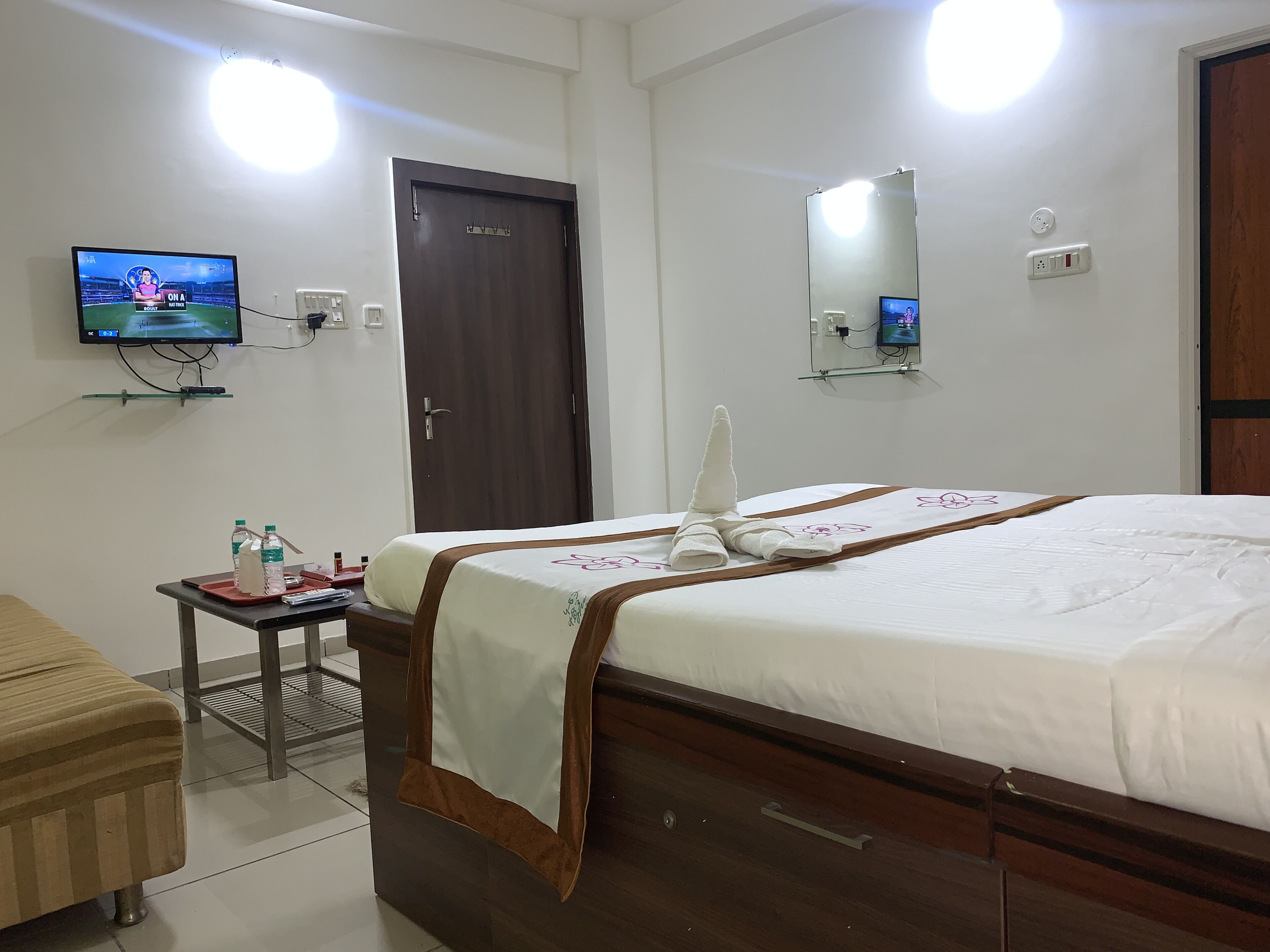 Habitació d'hotel amb un llit, una taula petita amb productes de tocador, una televisió penjada a la paret i una porta.
