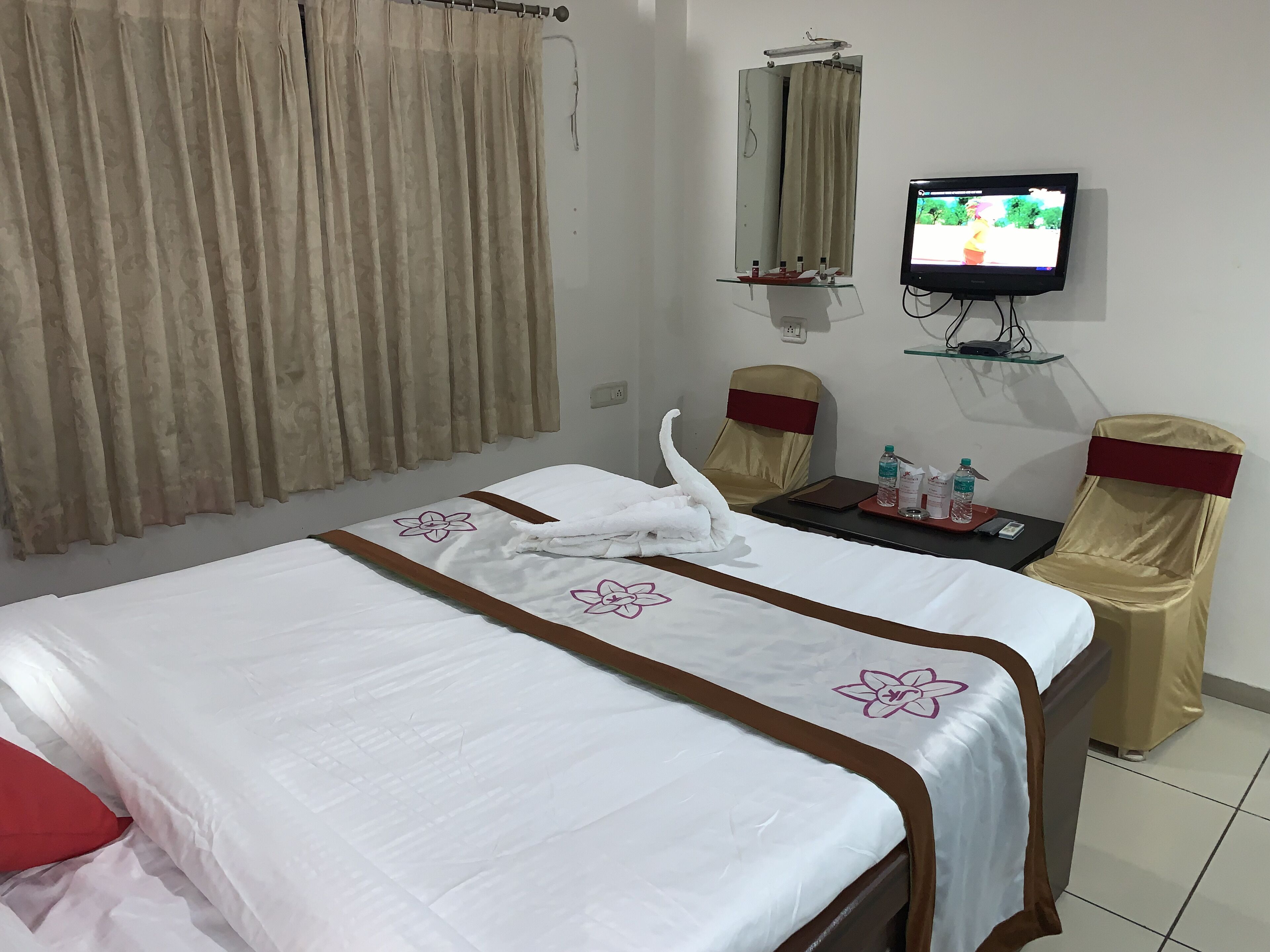 A hotel room with a bed, a desk, a chair, a television, and a mirror.