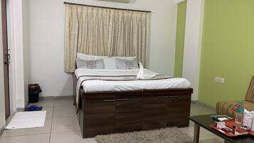 A neatly arranged bedroom with a bed, a bedside table with toiletries, a trash bin, and a green wall.