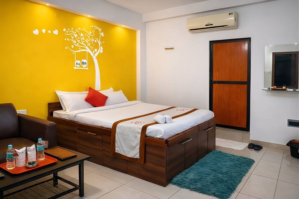 Una habitación de hotel con cama, escritorio, silla, baño y un diseño de árbol en la pared.