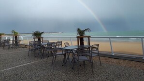An outdoor seating area with tables and chairs overlooking a beach, featuring a visible rainbow. - "La Fautaise" house in residence with swimming pool, near beach. (La Faute-sur-Mer)