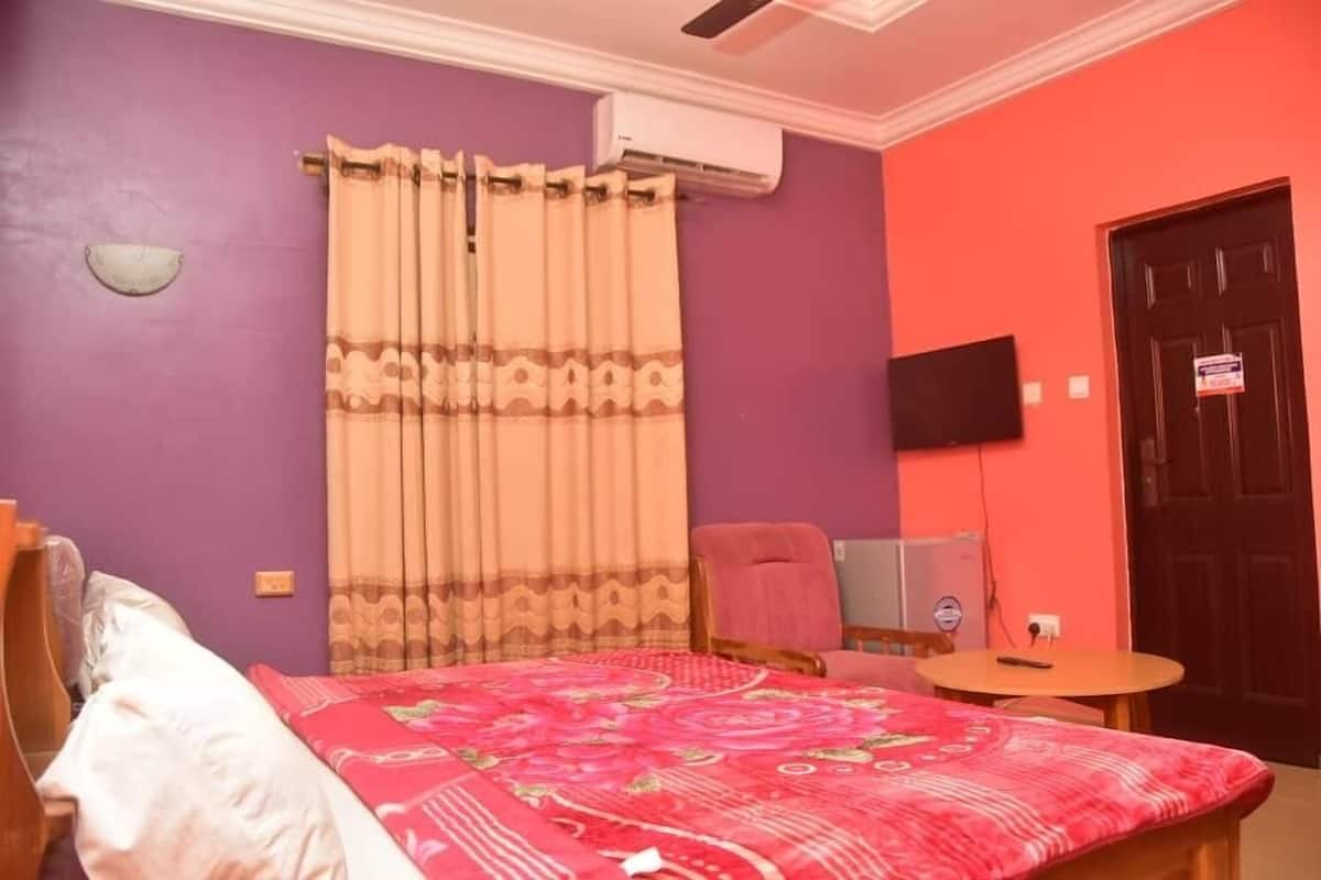 Ein Schlafzimmer mit Bett, Sessel, kleinem Tisch, Fernseher und Klimaanlage.