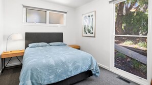 Une chambre à coucher comprenant un lit, des tables de chevet, un bureau, un ventilateur de plafond, une fenêtre avec des stores et un tableau encadré.