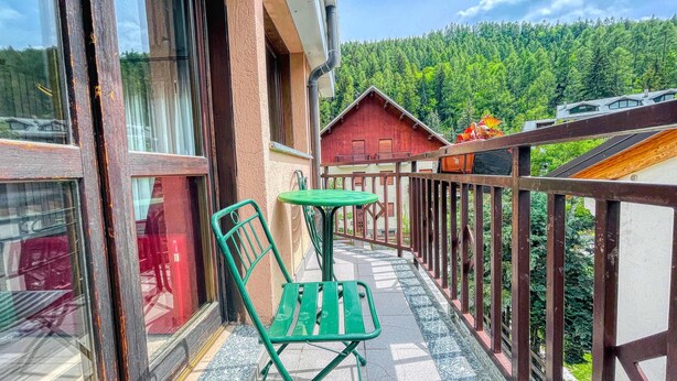 A balcony with a green chair and table, overlooking a forested area.