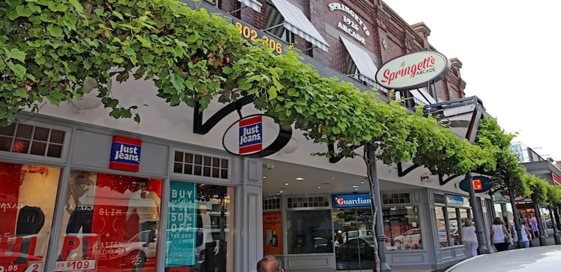 A storefront with a 'Just Jeans' sign, a 'Guardian' store, and a 'Springlett's Arcade' sign above.