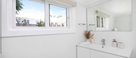 A modern bathroom with a large window, a white vanity, a mirror, and a view of a residential area.