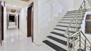 A modern hotel hallway with a staircase, white walls, and a tiled floor. - Hotel Bansidhar (Veraval)