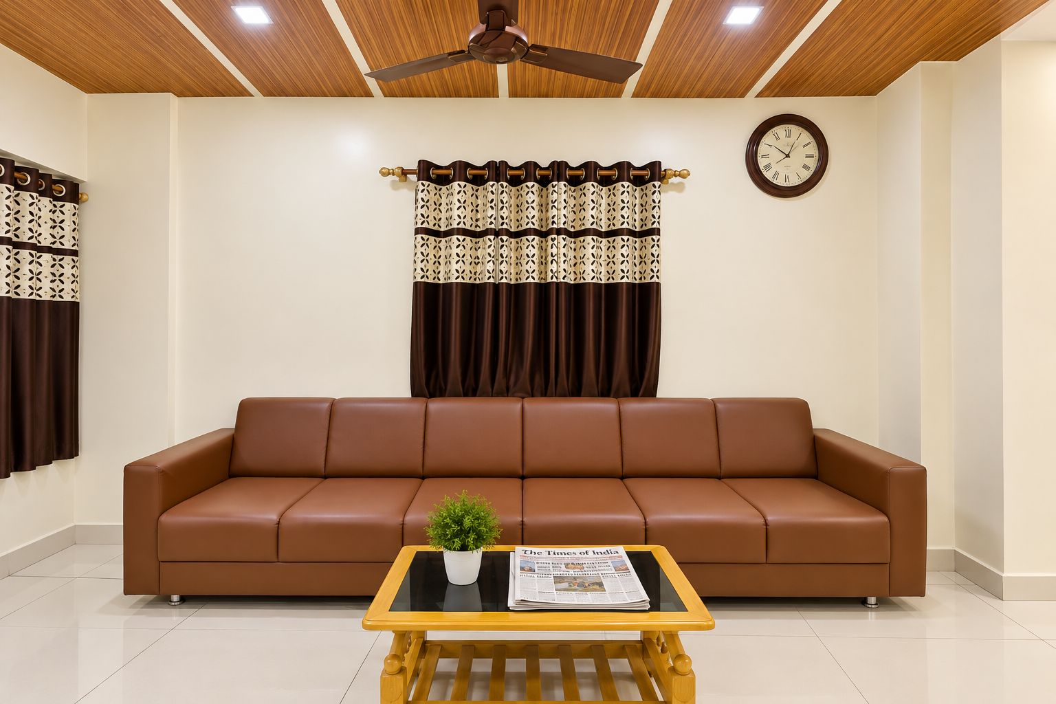 A living room with a brown leather sofa, a wooden coffee table with a newspaper, a potted plant, a ceiling fan, patterned curtains, and a wall clock.