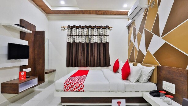 A modern hotel room with a bed, TV, and a small desk with a phone and glasses. - Hotel Bansidhar (Veraval)
