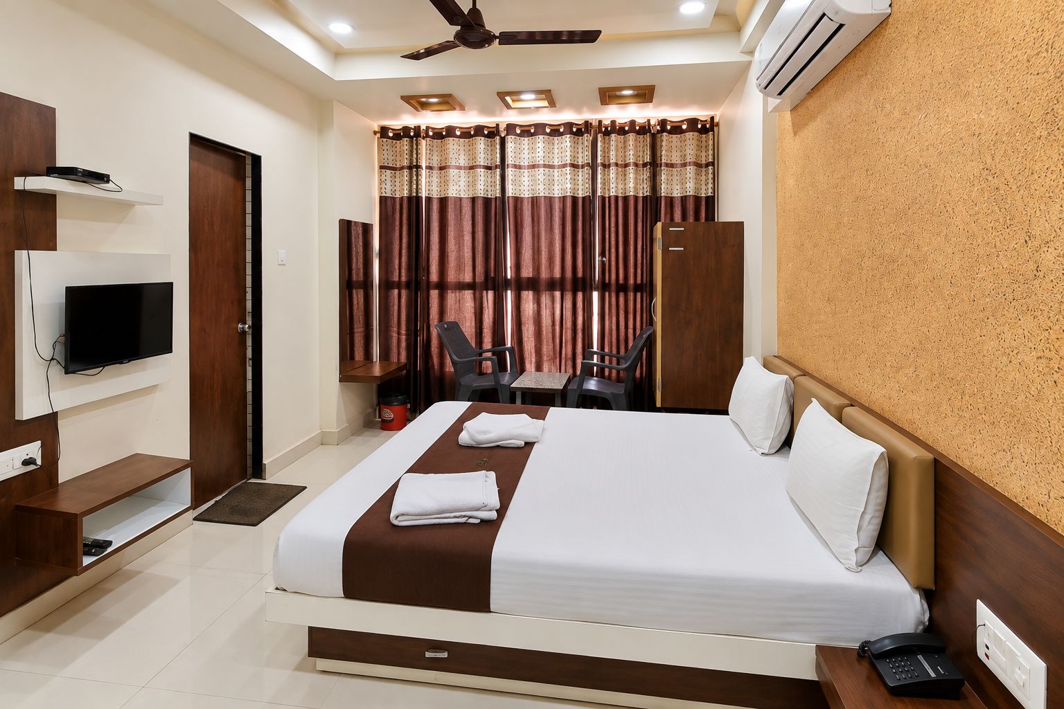 Een hotelkamer met een bed, televisie, bureau, stoelen en een airconditioner.