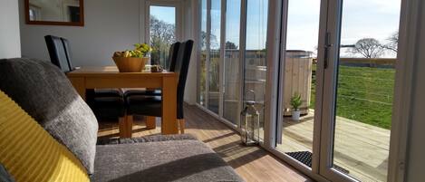 A modern living room with a sofa, a dining table with chairs, and a large sliding glass door leading to a balcony.