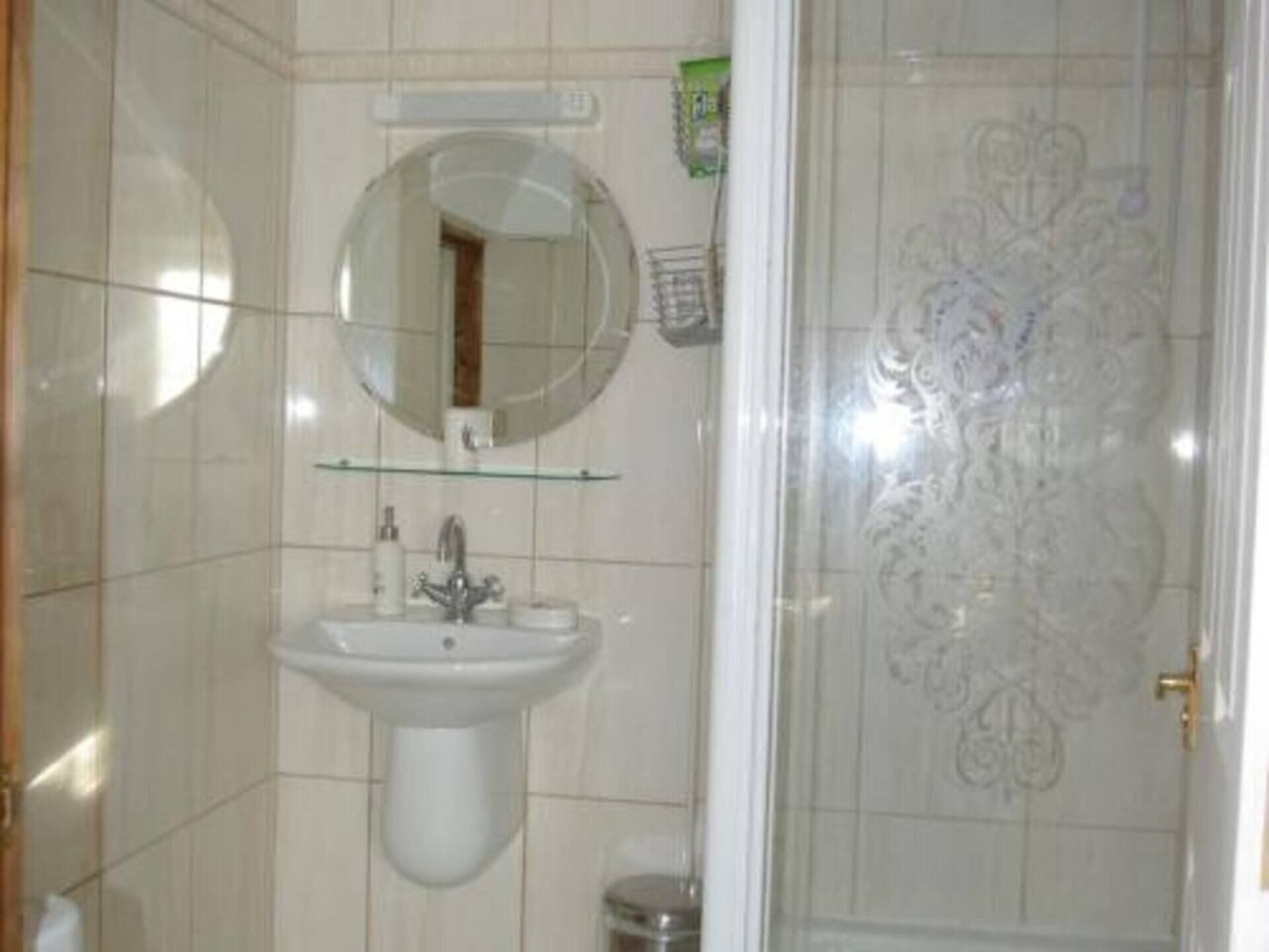 Een badkamer met een wastafel op voet, een ronde spiegel en een decoratieve deur.