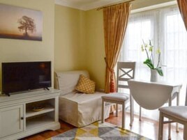 Uma sala de estar com televisão, sofá, poltrona, mesa pequena e um quadro na parede.