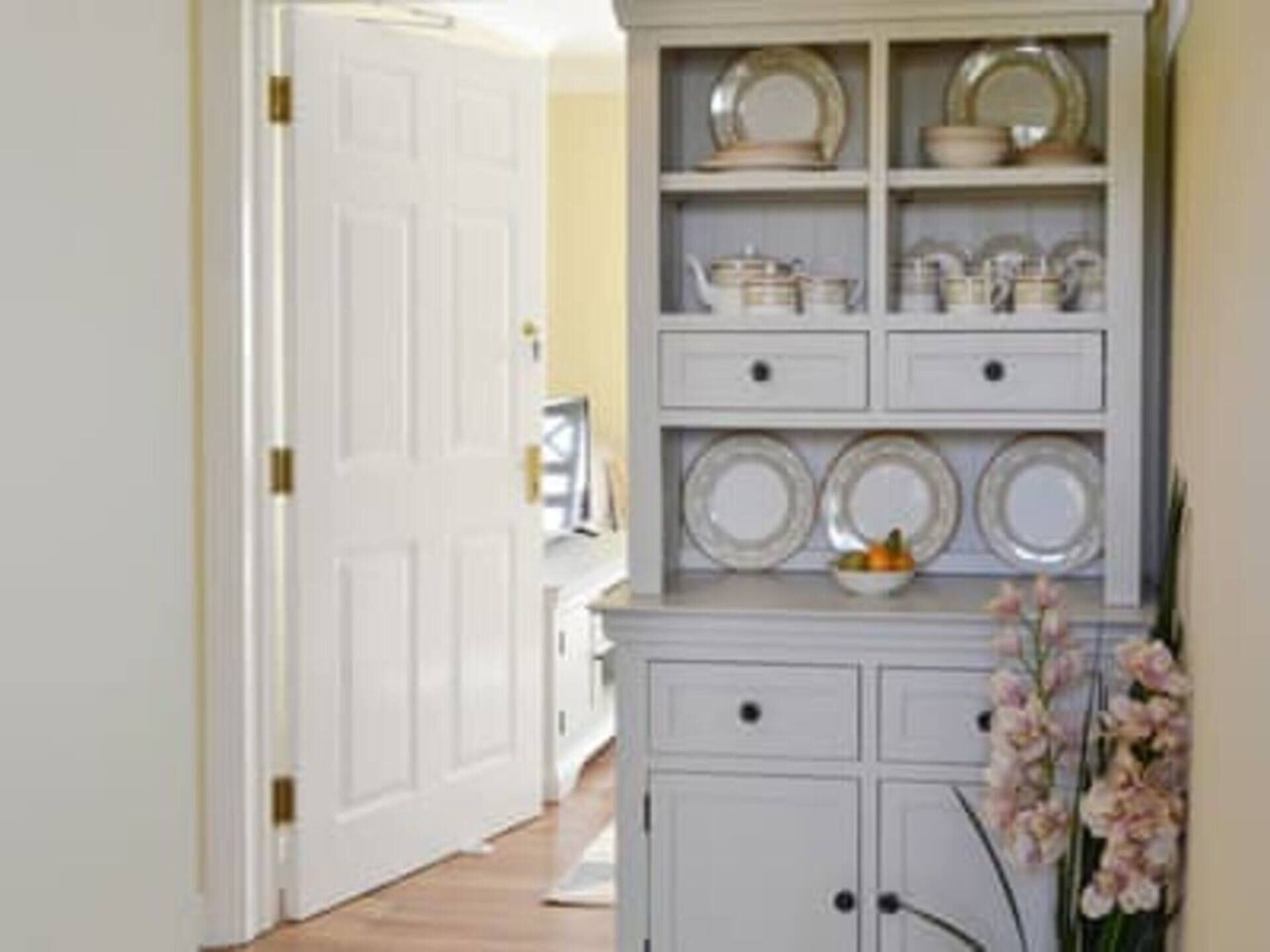 A hallway with a white door, a white cabinet with drawers, and a shelf with plates and bowls.