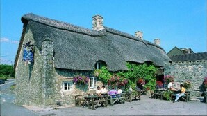 A traditional stone building with a thatched roof, a small window, and a sign on the side.