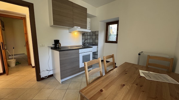 A compact kitchen with a built-in oven, a coffee maker, and a window. There is a wooden dining table with chairs.