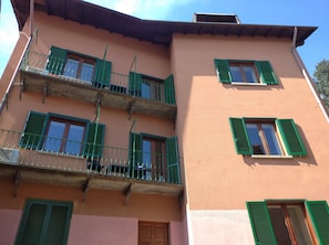 A multi-story building with balconies, green shutters, and a pink facade.