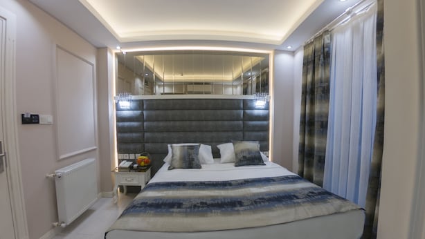 A modern bedroom with a curved headboard, a bedside table with a lamp, and a large mirror above the bed. - Crowned Hotel (Istanbul)