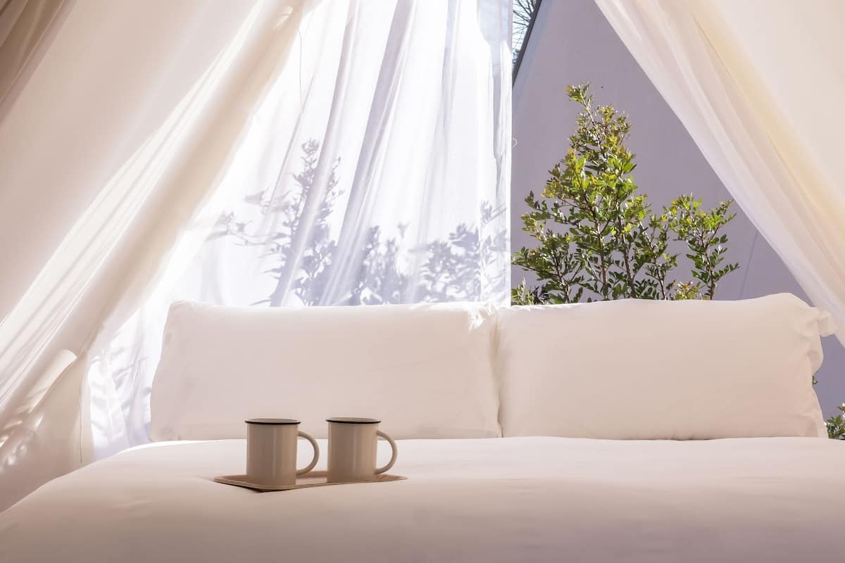 Un dormitorio acogedor con una cama, dos tazas y un ventanal con cortinas.
