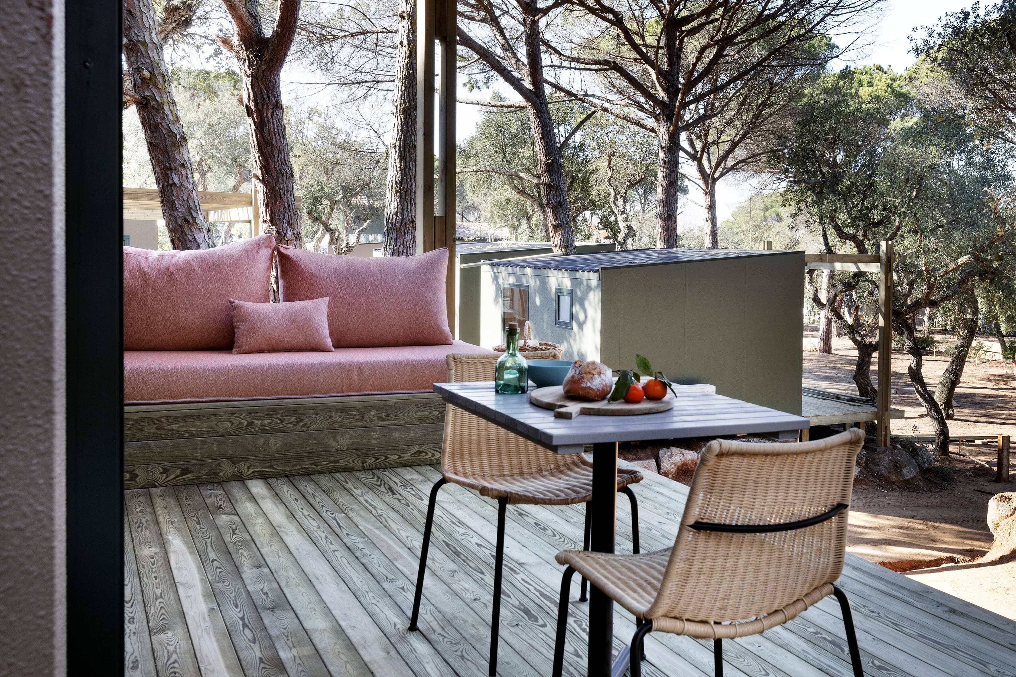 Une terrasse en bois avec une table, des chaises et un canapé rose.