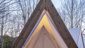 A triangular wooden tent with a bed inside, a lantern on the floor, and a woven basket. - wecamp Santa Cristina (Santa Cristina de Aro)