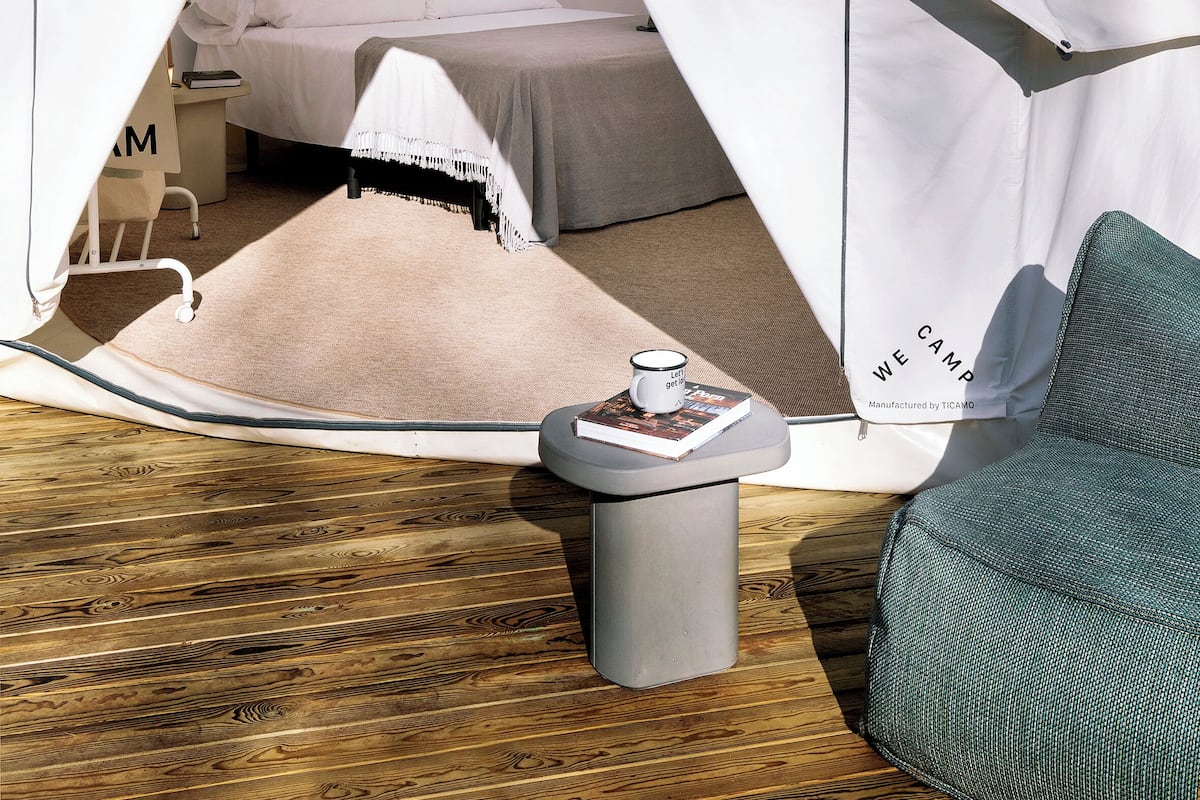 Una tienda de campaña con una cama en su interior, una mesita con una taza y una silla.