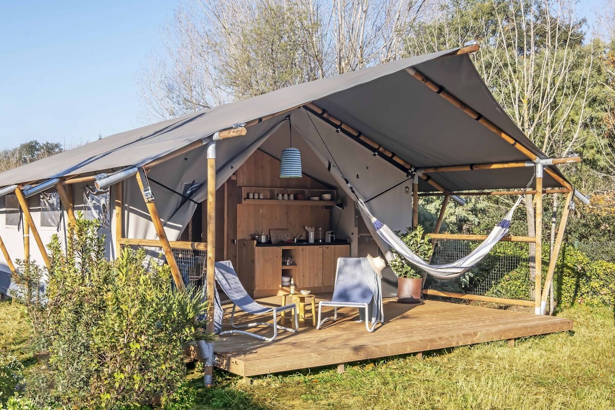 Una carpa acogedora al aire libre con una terraza de madera, una hamaca y una pequeña zona de cocina.