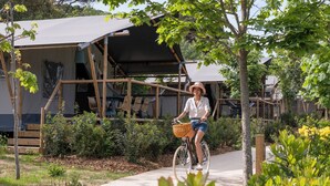 A person riding a bicycle on a paved path with a bamboo structure and greenery in the background. - wecamp Santa Cristina (Santa Cristina de Aro)