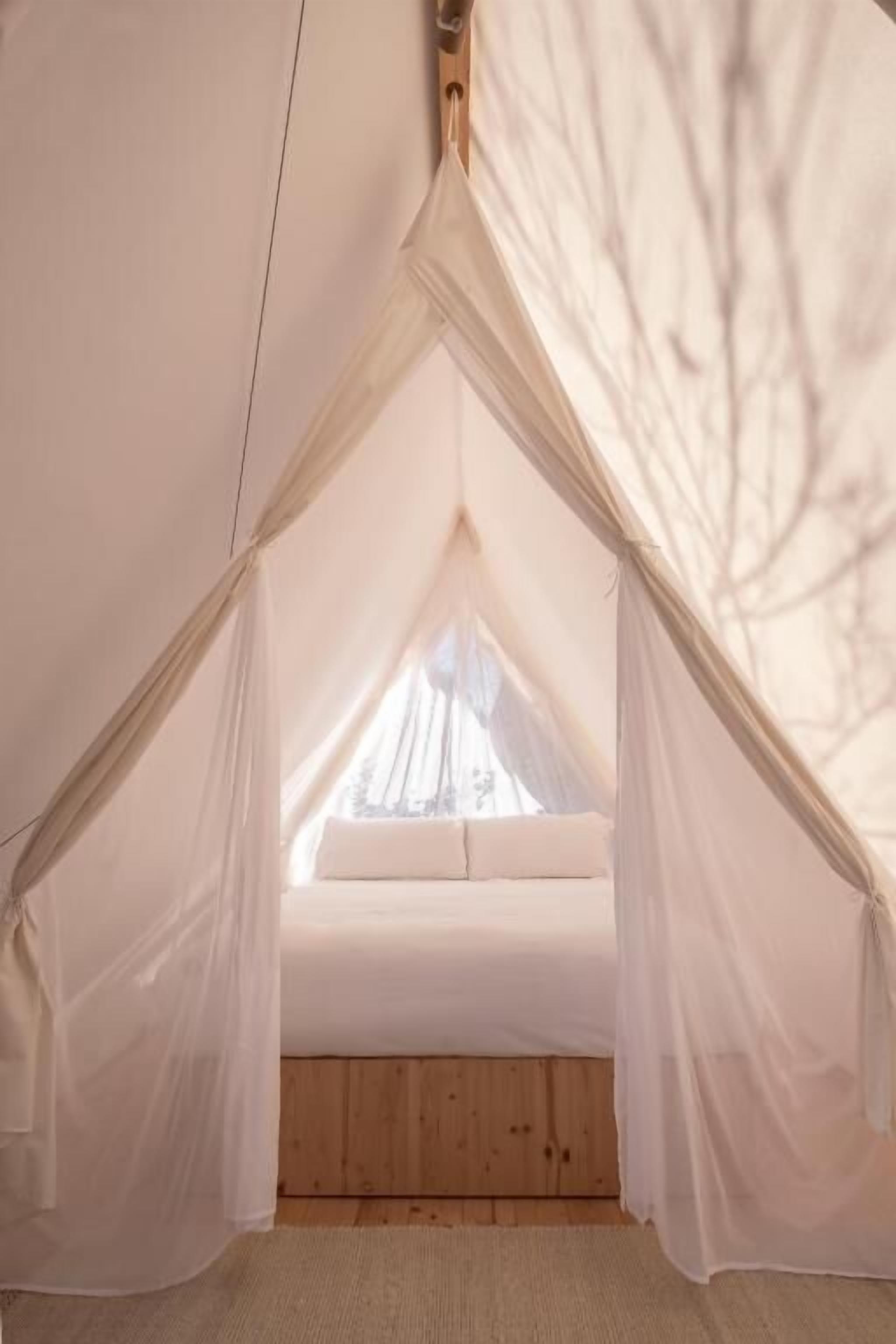 Un espacio tipo tienda de campaña con una cama y cortinas translúcidas.