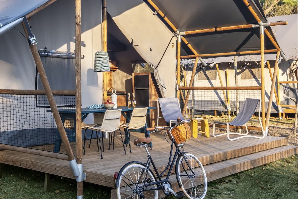 Una tienda de campaña con una terraza de madera, una bicicleta y mobiliario exterior.