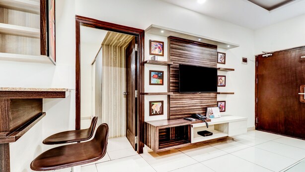 A modern living room with a wooden entertainment unit, a TV, framed artwork, and a brown leather chair. - Treebo Saga Apartment (Bengaluru)