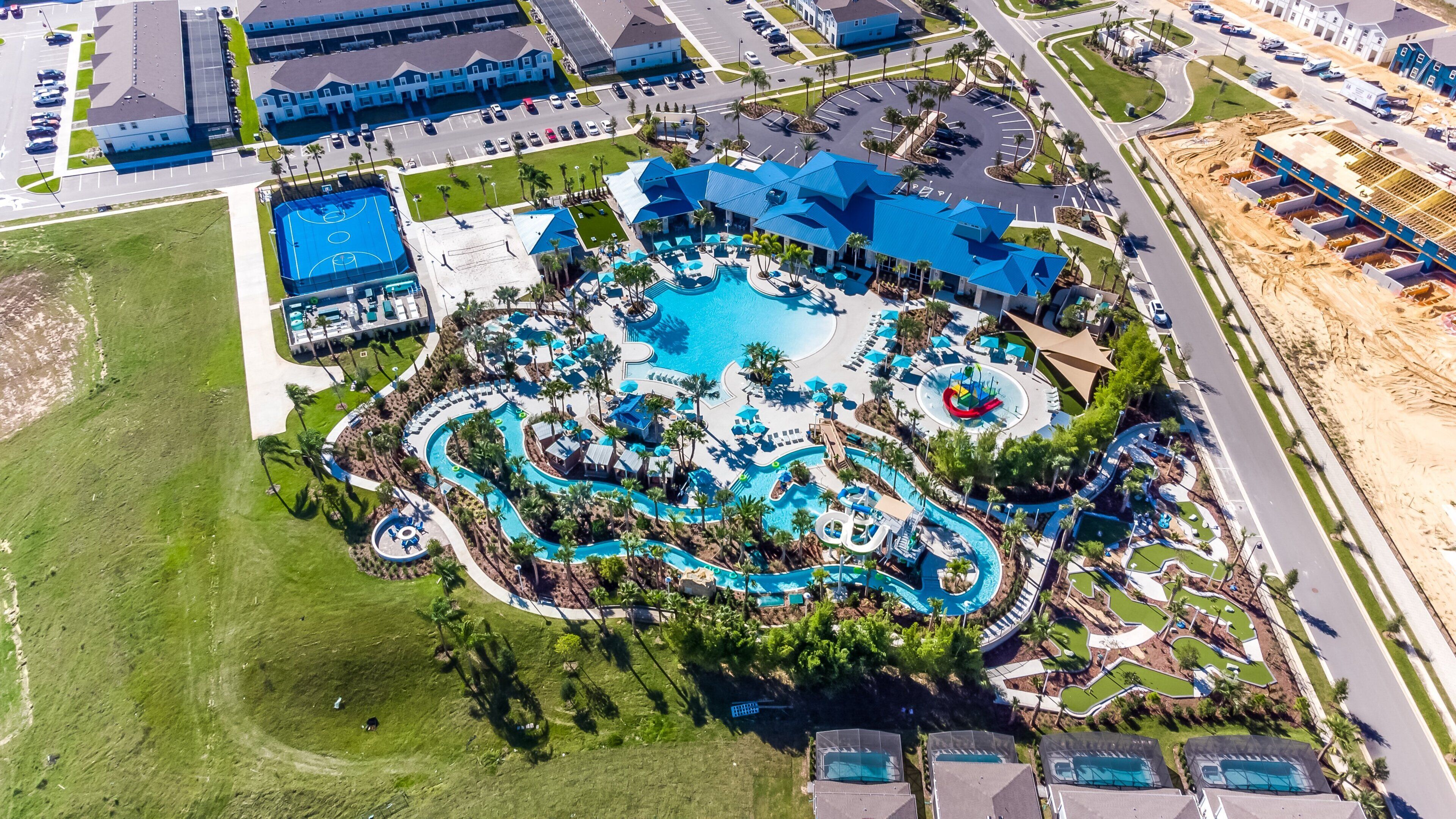 An aerial view of a resort with a central swimming pool, multiple guest rooms, and a parking area.