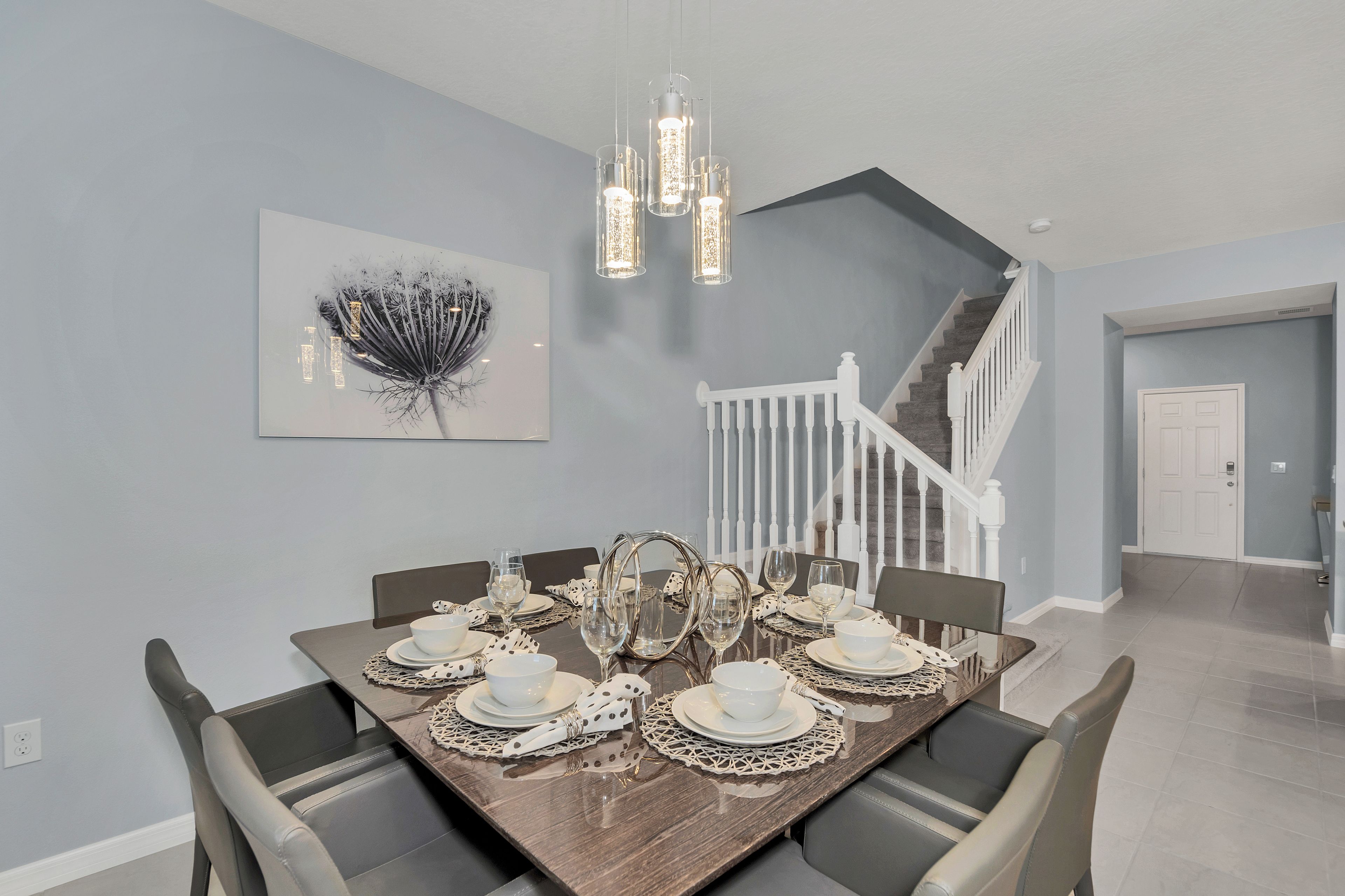 Un coin repas avec une table en bois dressée pour six personnes, des chaises blanches et un lustre.