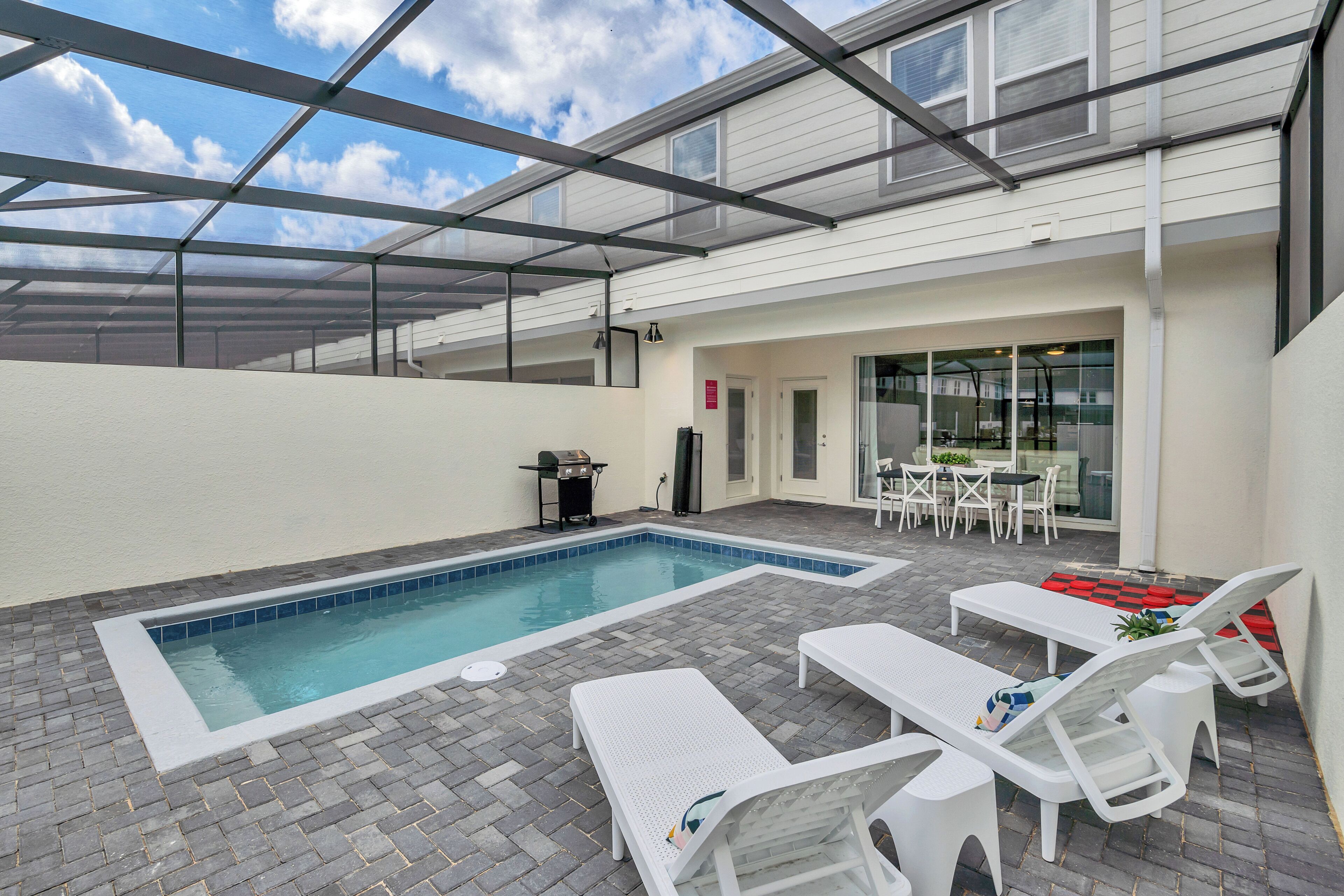 Piscina interior com cadeiras de descanso e uma mesa, rodeada por um terraço coberto.