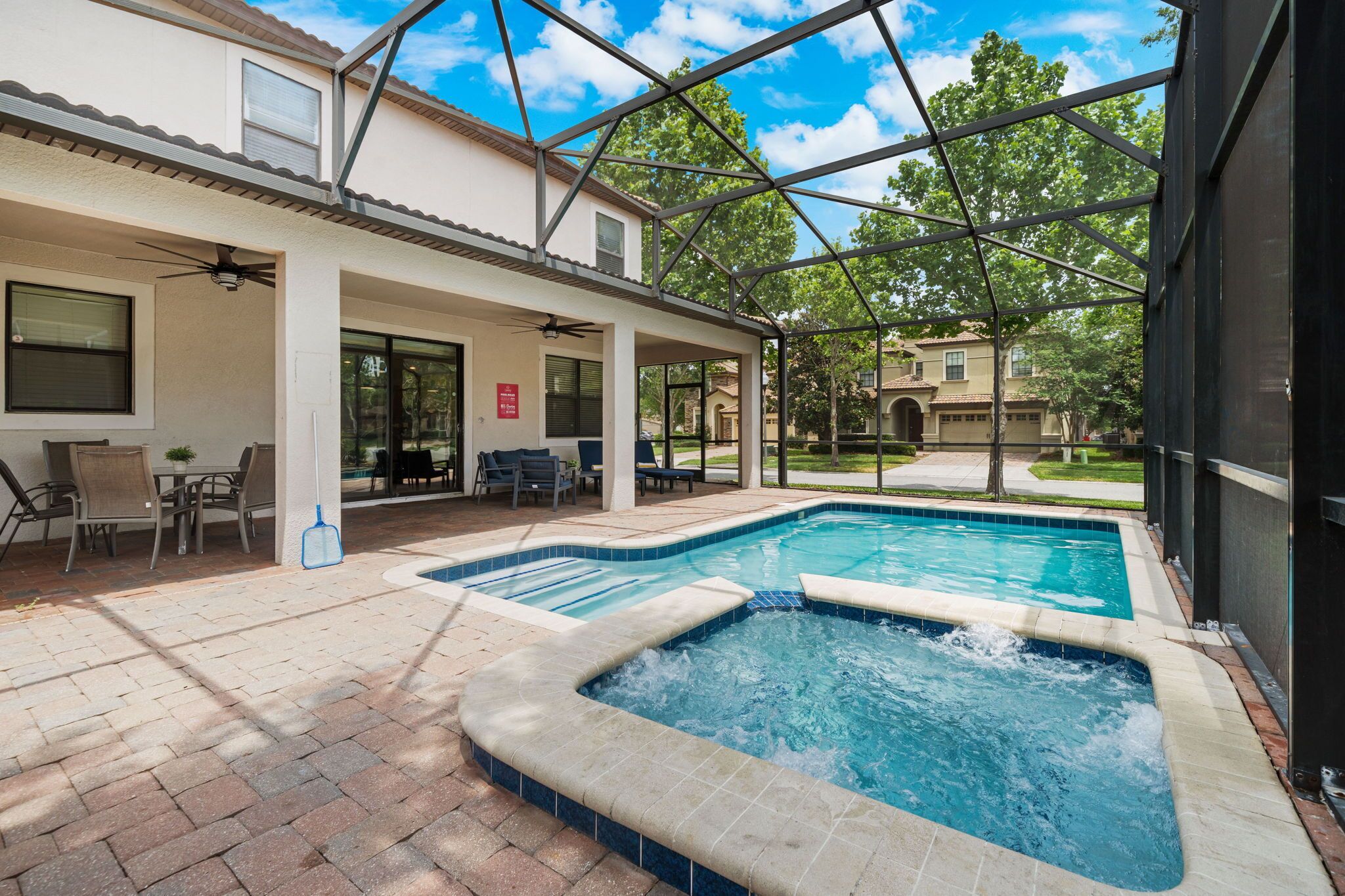 A covered outdoor swimming pool area with a hot tub, patio furniture, and a view of the neighborhood.