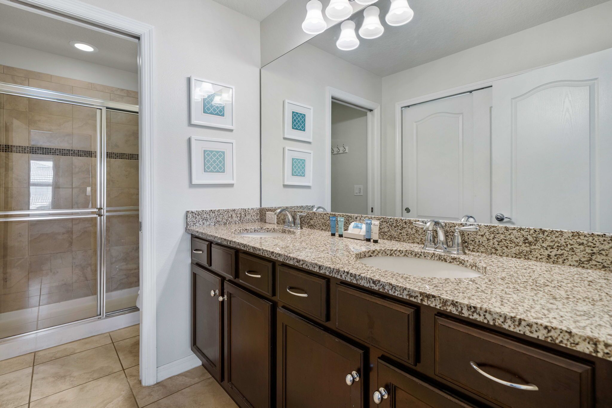 A bathroom with a double sink, dark wooden cabinets, a large mirror, and a shower area.