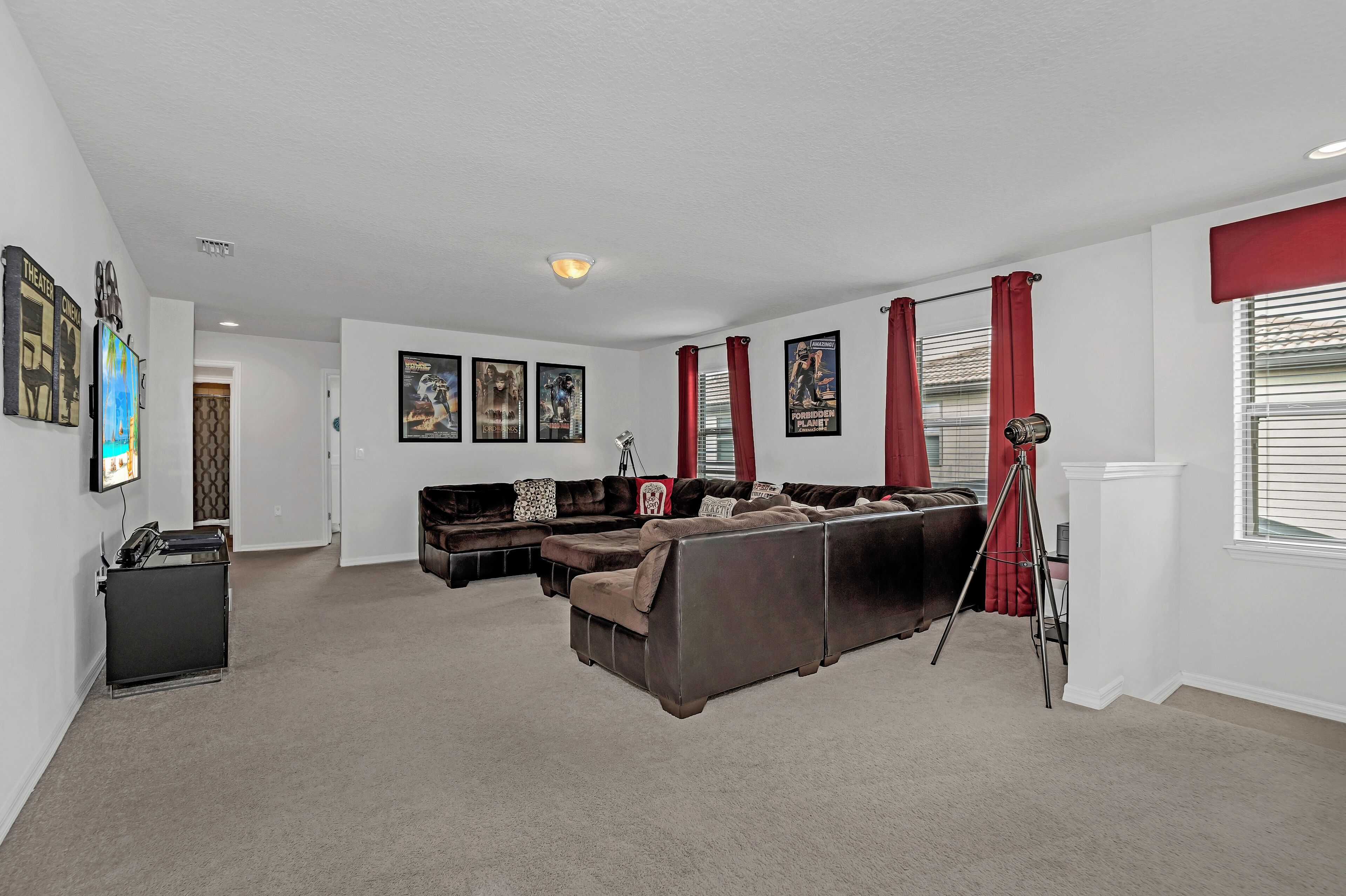 A living room with a sectional sofa, a tripod stand, and framed movie posters on the wall.