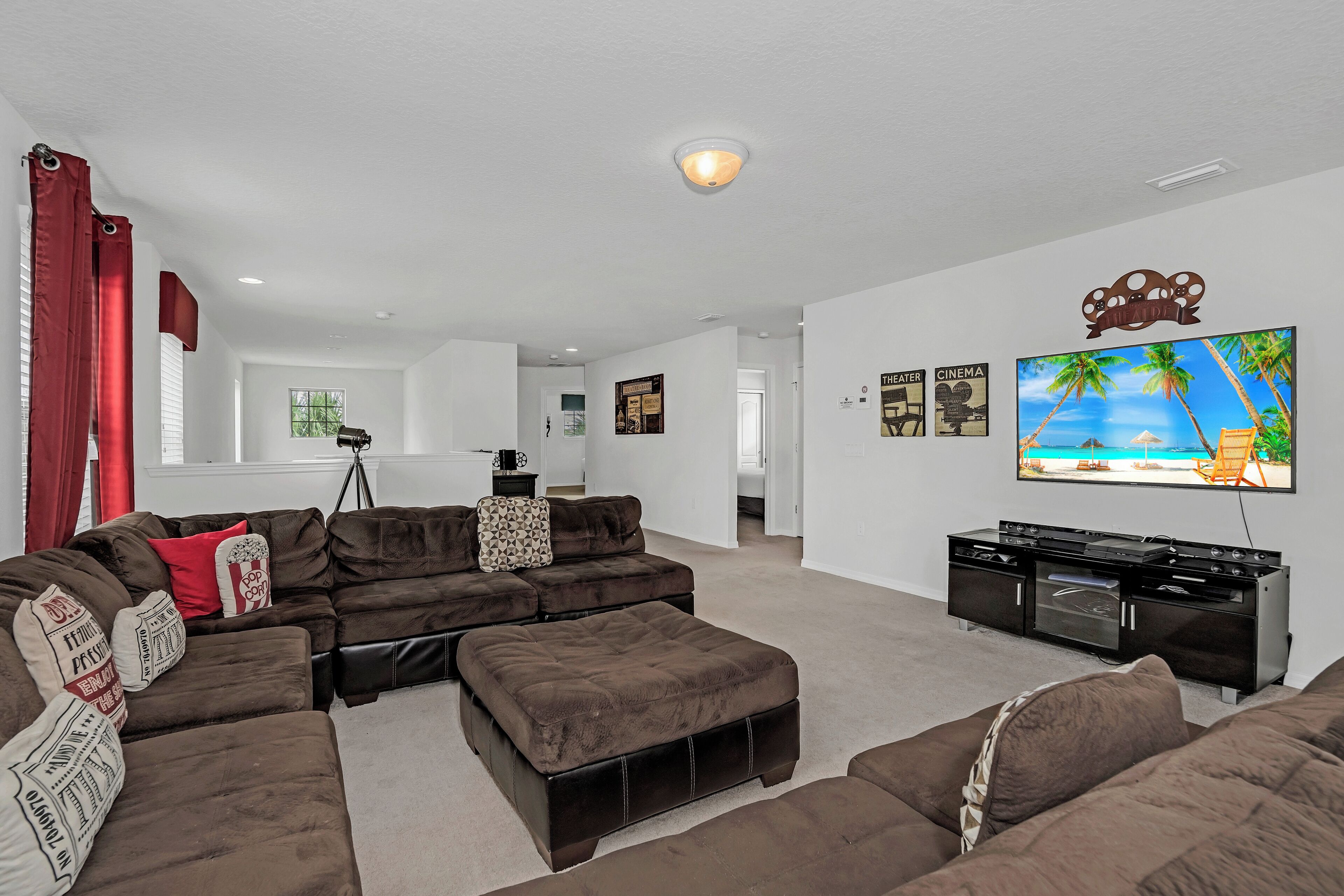 A living room with a sectional sofa, a flat-screen TV mounted on the wall, and a kitchenette area.