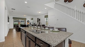 A modern kitchen with granite countertops, a double sink, and a dining area with a table and chairs. - Elegant Villa W/private Pool/spa & Game Room! (Kissimmee)