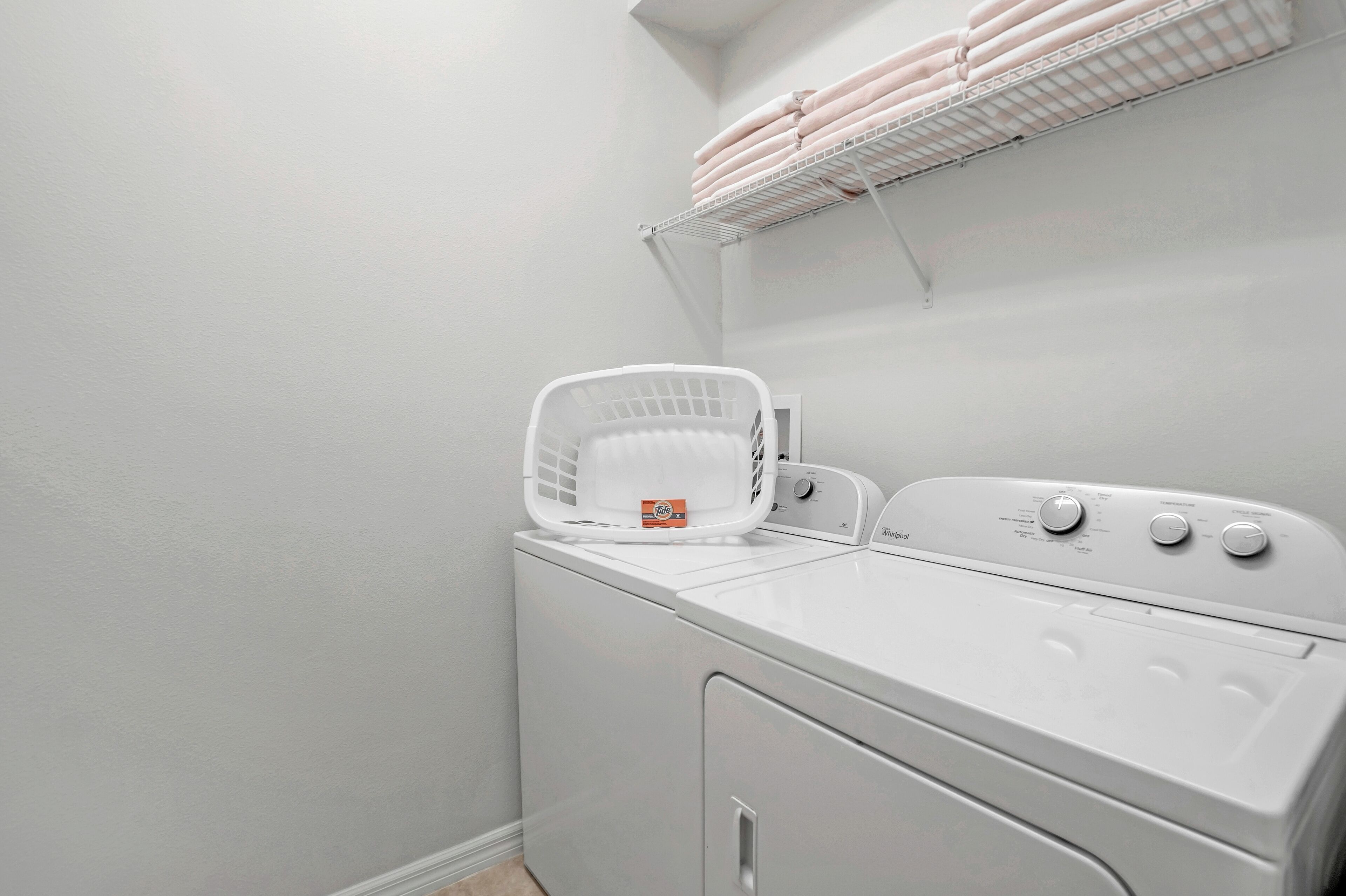 A laundry area with a white washing machine, a white dryer, and a white laundry basket.