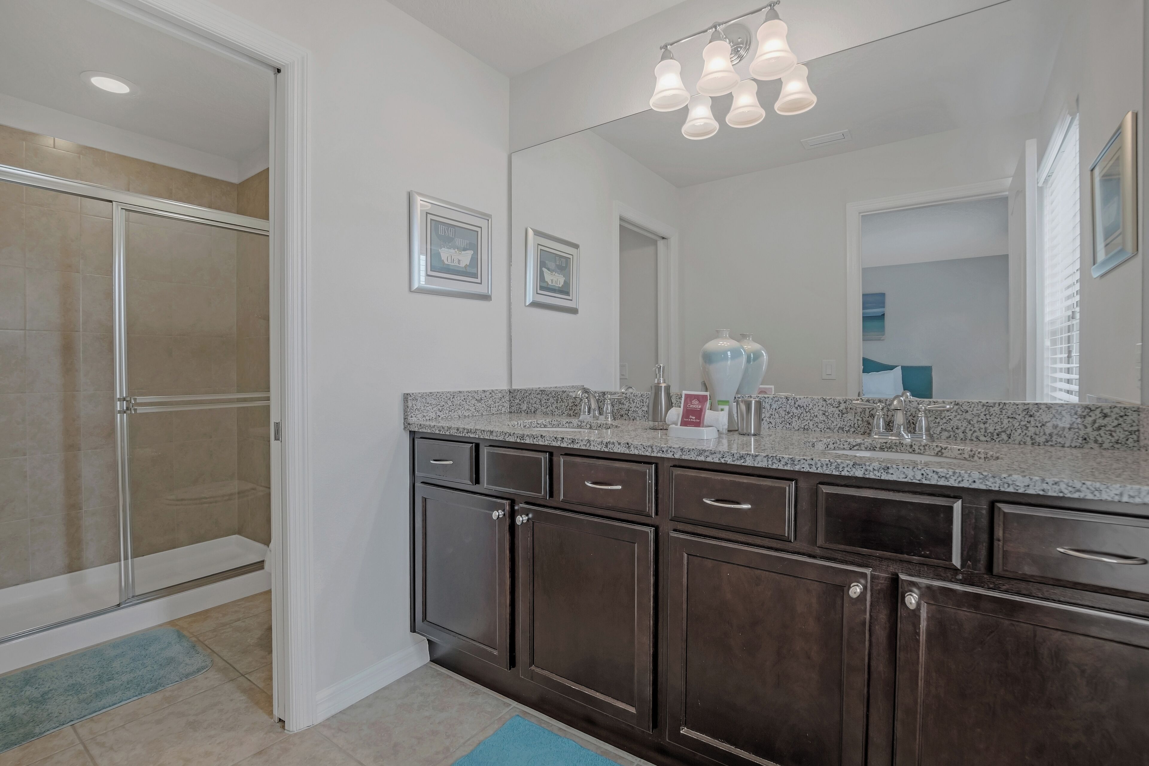 A bathroom with a large mirror, dark wooden cabinets, a granite countertop, and a shower area.